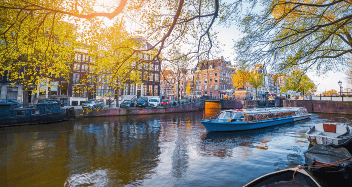 Scenic photo of a canal in Amsterdam, a canal boat, bridge and houses beside the water on a sunny day