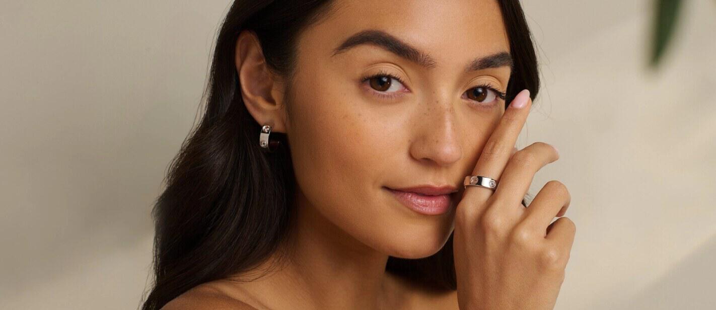 how to save money at Clogau guide - A woman wearing silver earrings holding a finger with a ring on it to her face